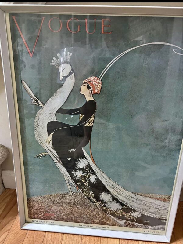 Framed vintage Vogue magazine cover shows a woman in an ornate black dress and red headdress seated side-saddle on a white peacock against a teal background. Art deco style, dated November 15, 1911, with elegant, stylized detailing and bold VOGUE title at the top.