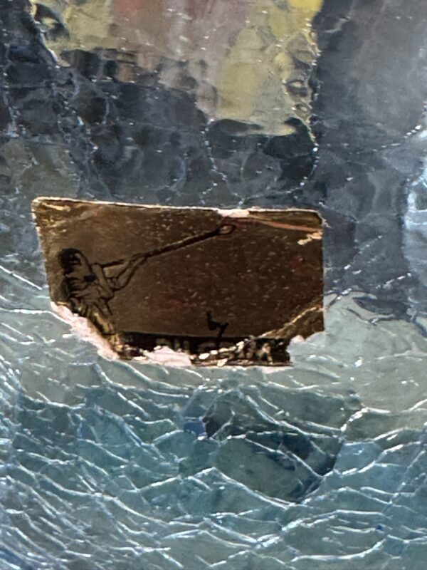 A close-up of a textured blue and clear glass surface with a small torn gold sticker. The sticker features a black illustration of a person holding a long stick or spear, pointing it diagonally upward to the left. The sticker is partially damaged and peeling.