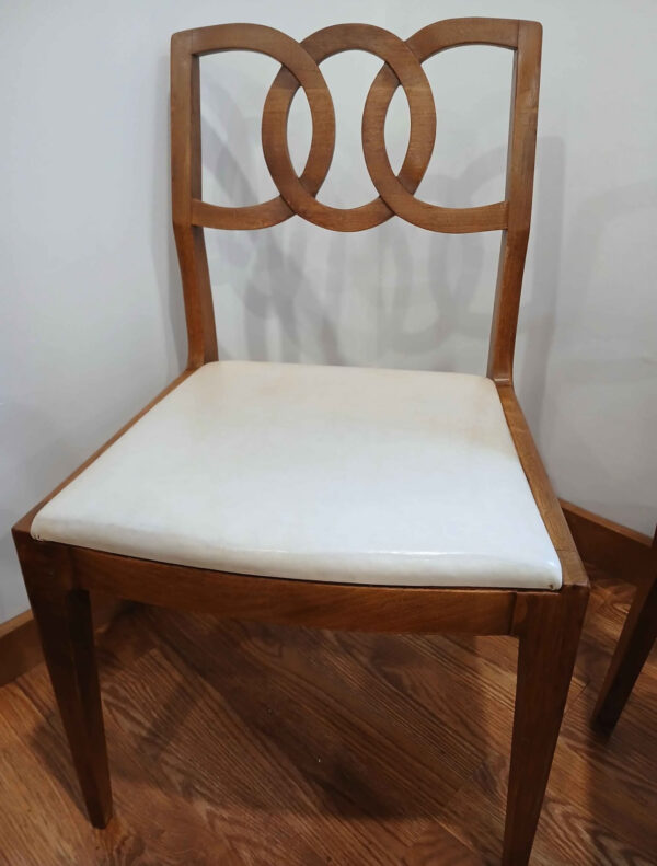 A wooden chair with a white cushioned seat and a distinctive backrest featuring two interlocking circles, placed on a wooden floor against a plain wall.
