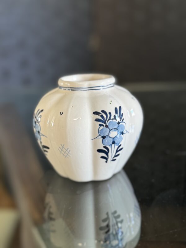 The English Ivy Teacup is a small, round, white ceramic vase with vertical grooves, hand-painted blue flowers and leaves, simple geometric accents, and a flared opening, evoking the charm of a delicate teacup.