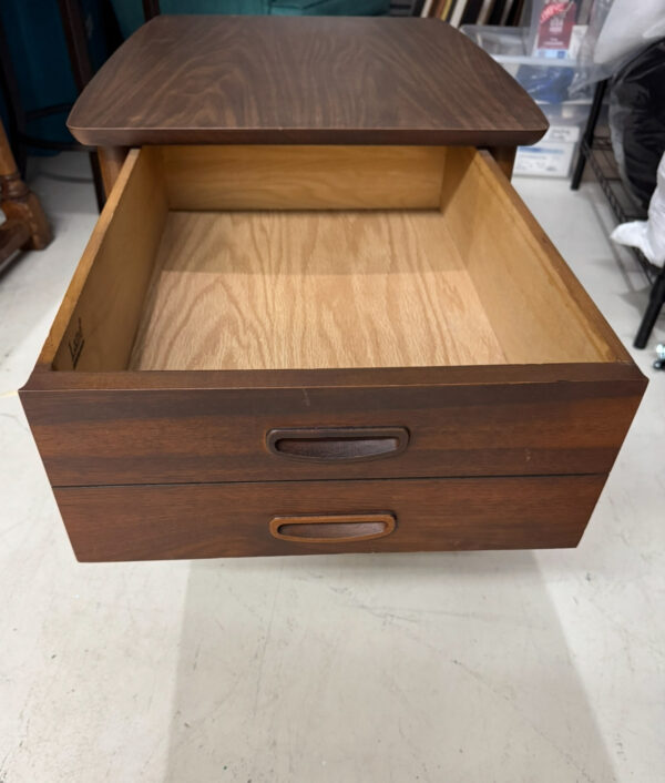 A pair of Lane Side Tables, each featuring two drawers. One table is displayed with its top drawer open to show the empty, light wood interior; the lower drawer is shut. The tables stand on a light floor with room decor in the background.