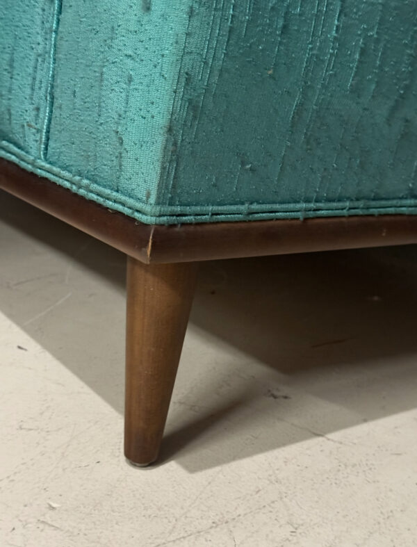 Close-up of a teal Kroehler Wingback Chair Set with textured, slightly worn upholstery and a tapered wooden leg showing wear at the foot, resting on a light floor and highlighting the vintage charm of Kroehler furniture.