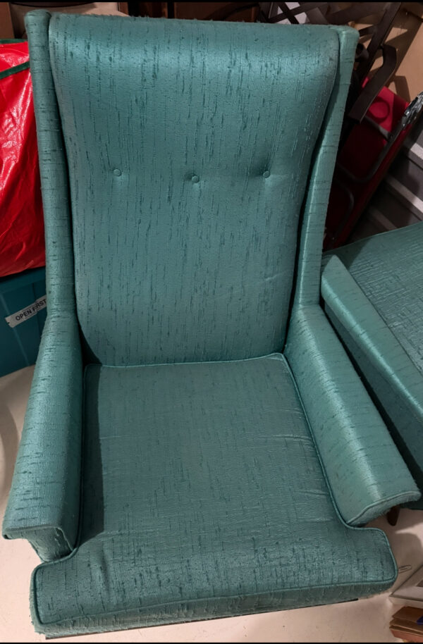 A teal Kroehler Wingback Chair Set with textured upholstery, tall sides, two backrest buttons, and wide, sloping armrests sits on a light floor near a cushion, with red and blue items visible in the background.