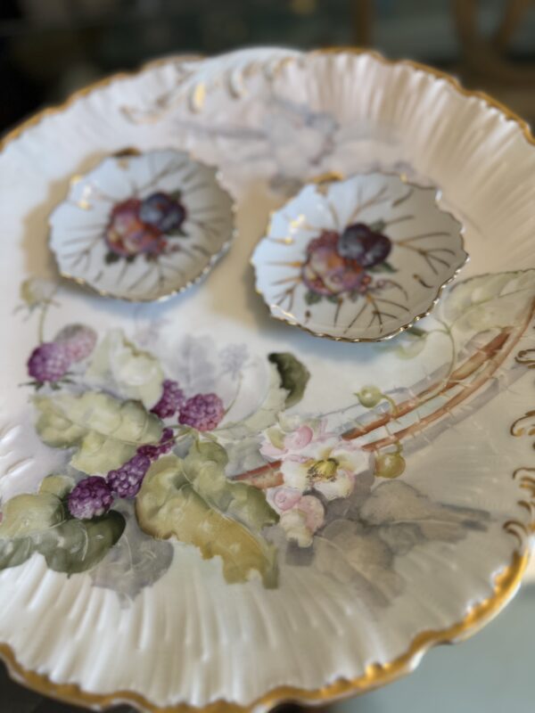 Hand-Painted M. Redon Plate c. Late 1800s with a scalloped, gold-edged rim and floral and fruit designs, including grapes and leaves; two smaller matching dishes rest on the plate, forming a face-like display.