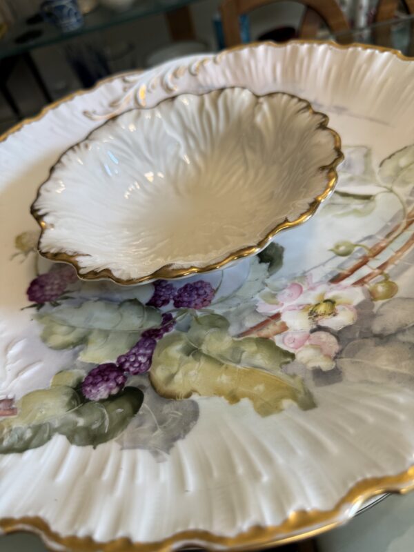 A close-up of the Hand-Painted M. Redon Plate (late 1800s) shows ornate scalloped edges, gold trim, and a detailed floral and fruit design, with a smaller rippled bowl displayed on top.