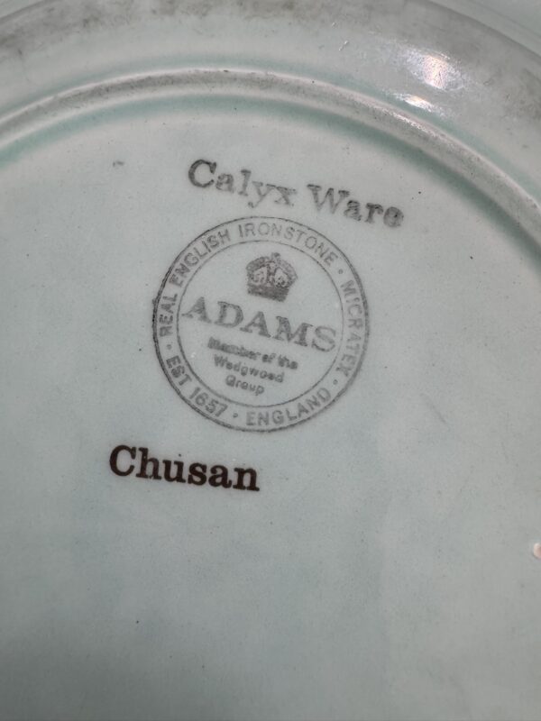 Close-up of the underside of a pale ceramic plate showing a stamp that reads “Calyx Ware,” “ADAMS,” “Real English Ironstone,” “Microwave Safe,” “Wedgwood Group,” “ESTD 1657 ENGLAND,” and “Chusan” in brown text.