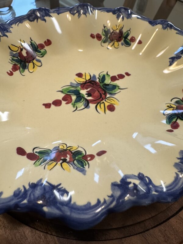 A yellow ceramic plate with a scalloped blue rim, decorated with colorful hand-painted floral designs in red, yellow, and green. The plate features one large central floral motif and four smaller flowers evenly spaced around the edge.