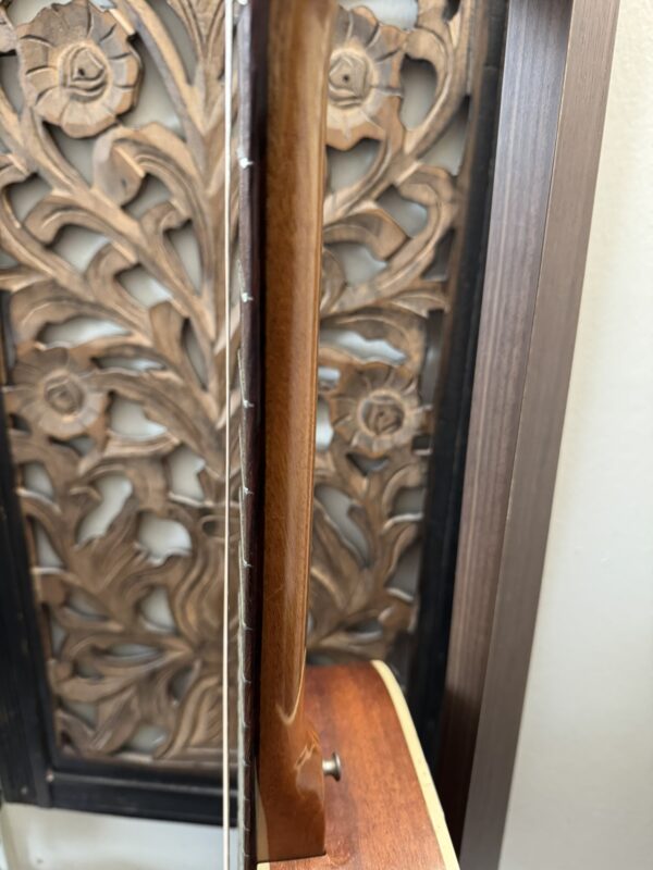 A close-up side view of a Silvertone 1960's 699 Guitar neck and headstock, showcasing its strings and wood grain, with ornate wooden floral carvings on the left and the guitar featured on the right.