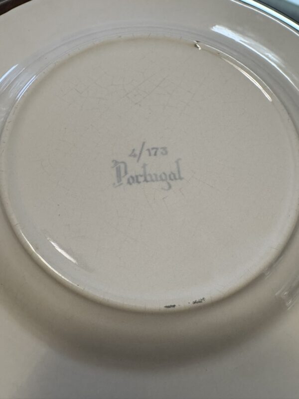The underside of a ceramic plate shows a faint blue stamp reading 4/173 Portugal in stylized text. The plate has a slightly raised base and visible crazing lines in the glaze, indicating age or wear.