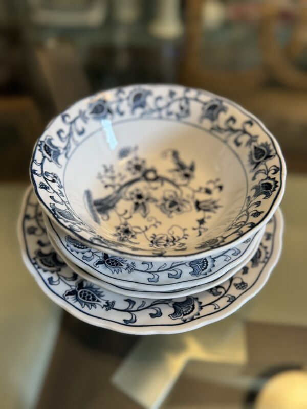 A stack of three white ceramic bowls with blue floral and vine patterns sits on a glass table. The bowls have detailed, intricate designs along the rim and center, and the background is softly blurred.