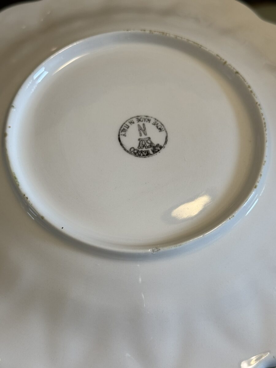 The image shows the bottom of a white ceramic plate with a black stamp mark in the center reading N, Made in Italy, Florence arranged in a circular pattern around a crest-like emblem. The plate has a raised base ring and some minor glaze imperfections around the edges.