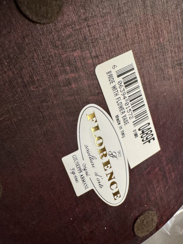 Close-up of the underside of the Armani Bride Figurine showing two stickers: an oval one marked FLORENCE sculture d’arte, Giuseppe Armani, 1993, and a barcode label reading BRIDE WITH FLOWER AGE, Made in Italy. Two round felt pads are also visible.