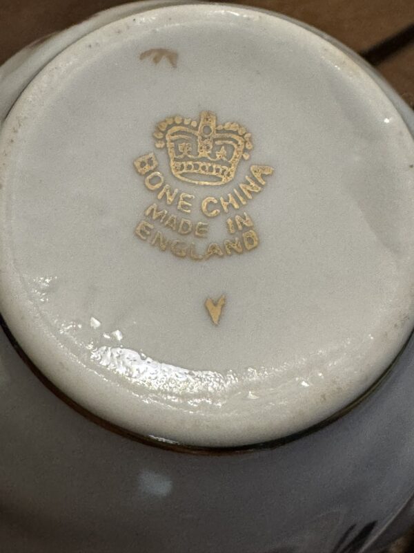 The bottom of a white porcelain dish shows a gold crown emblem stamped above the words “BONE CHINA MADE IN ENGLAND.” Below the text is a small gold “V” mark. The surface appears glossy with some subtle reflections.