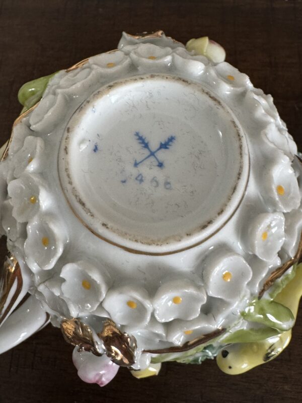 A close-up of the underside of a Meissen Schneeballen Cup shows ornate white flower designs with yellow centers at the base, and the blue Meissen crossed-swords mark with the number 456 visible against a wooden background.