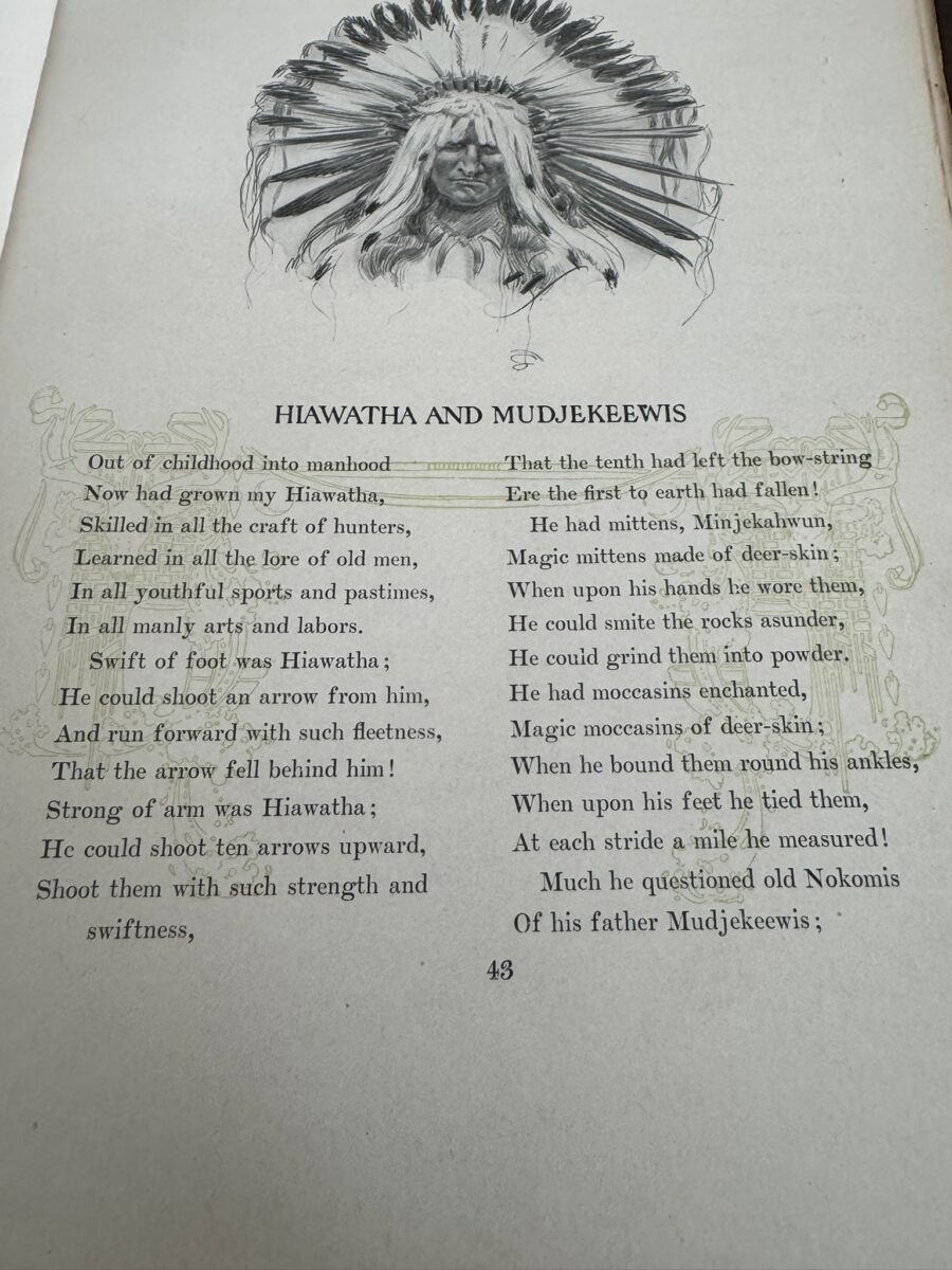 A page from a vintage book shows a poem titled Hiawatha and Mudjekeewis beneath an illustration of a Native American chief in a feathered headdress. Decorative borders frame the poem, which is printed in a serif font on aged, yellowed paper.