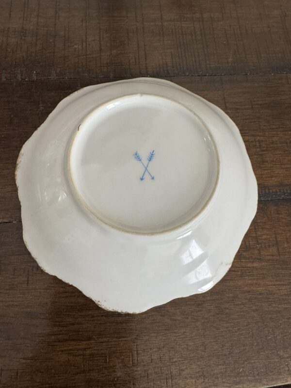 A Woulind Chile Serving Dish made of white porcelain rests upside down on a wooden surface, featuring a scalloped edge, blue crossed-swords mark at the base, and slightly worn, discolored rim and edges.