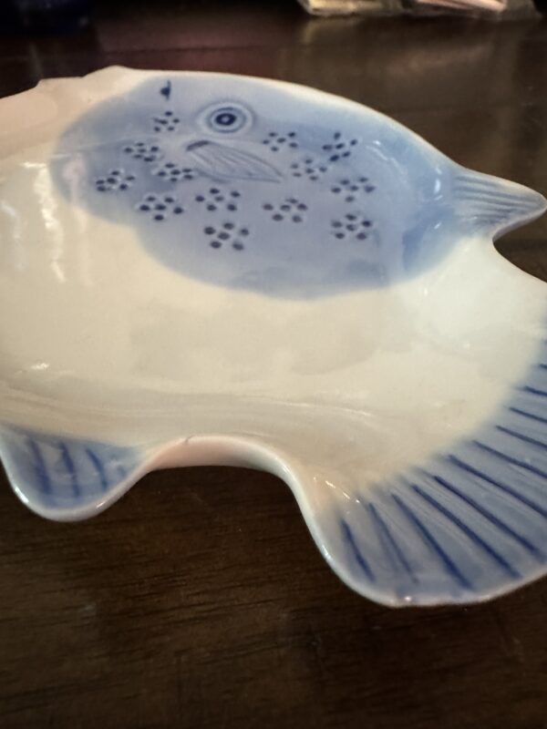 The Woulind Chile Serving Dish is a blue and white ceramic piece shaped like a fish with a round body, detailed fins, and dotted patterns, adding style to any table or dark wooden surface.