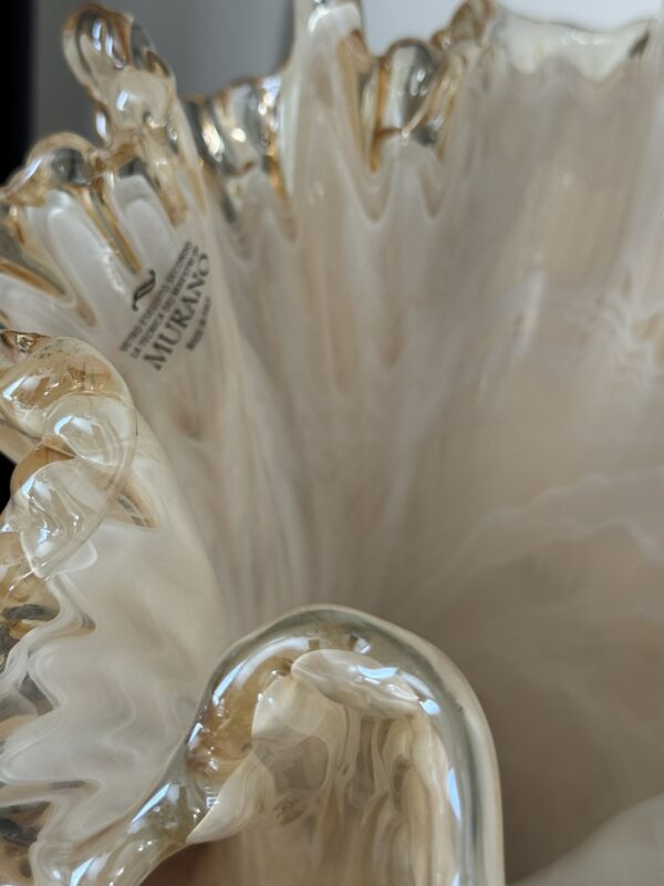 A close-up of the Woulind Chile Serving Dish features wavy, ruffled edges in creamy white and gold. Labeled “Murano,” it showcases Venetian craftsmanship with glossy, translucent folds that beautifully catch the light.