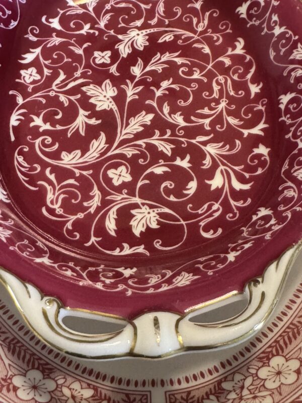 Close-up of the Woulind Chile Serving Dish, featuring a maroon and cream floral vine pattern. The ornate border has cutouts and gold accents, while textured leaves and flowers enhance its intricate design.