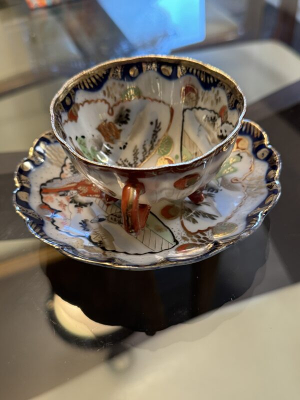 A close-up of the Woulind Chile Serving Dish, adorned with blue, red, and gold floral and geometric patterns, a scalloped rim, and elegant gold accents, set on a reflective glass table.