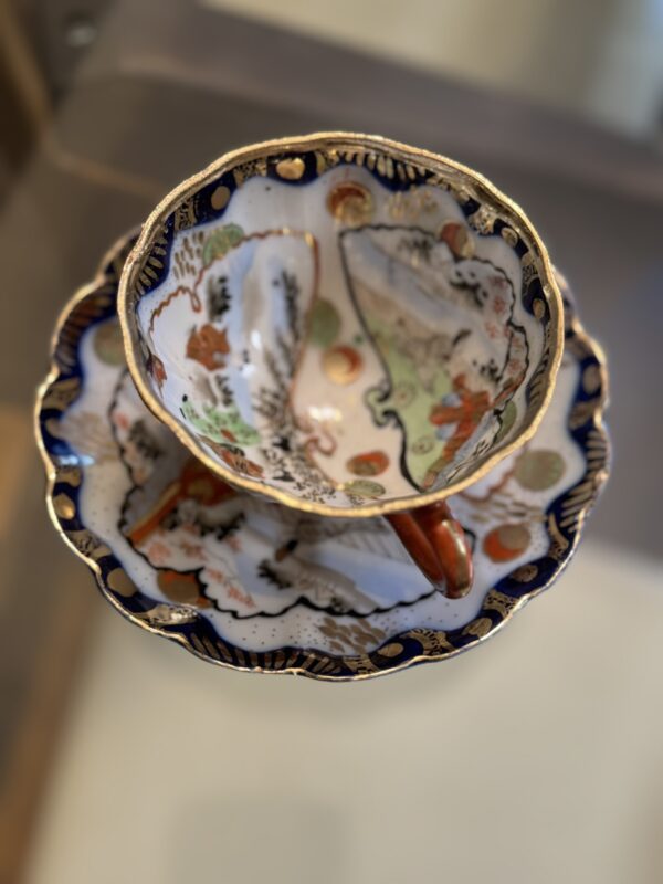 A porcelain teacup and saucer with scalloped edges, gold accents, and hand-painted floral and landscape designs. Perfectly pairs with the Woulind Chile Serving Dish for an elegant table setting.