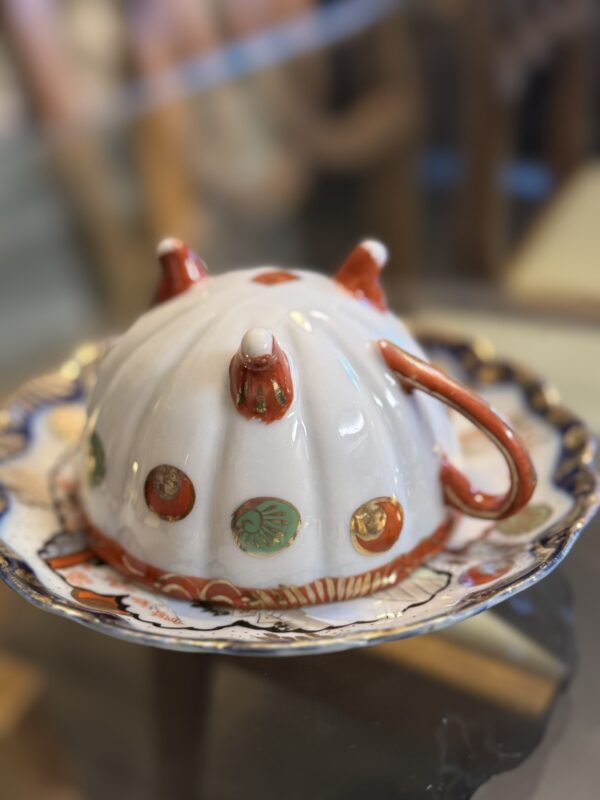 The Woulind Chile Serving Dish is a ceramic butter dish with a domed white lid, orange handles, green circles, and a plate featuring a blue and gold scalloped rim—perfect for serving or as décor.