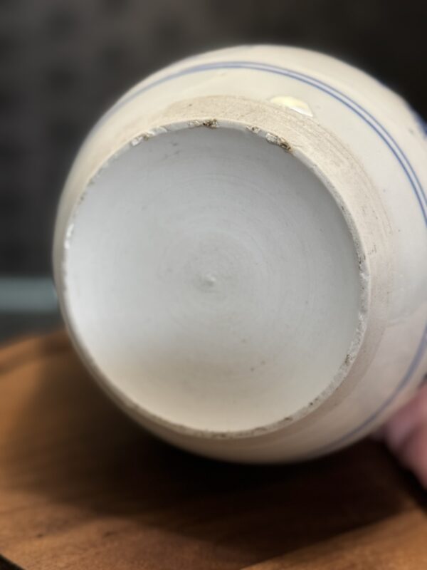 A close-up of the underside of a Woulind Chile Serving Dish shows its smooth white ceramic base, several small chips on the rim, faint blue lines above the base, and a wooden surface visible underneath.