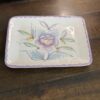 The Woulind Chile Serving Dish, a small rectangular ceramic tray with rounded edges and a scalloped purple border, displays a pastel floral design in purple, pink, blue, and green as it sits on a wooden table.