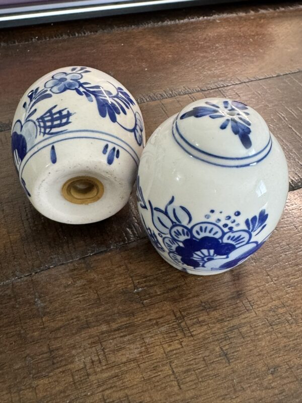 Two Woulind Chile Serving Dishes, with blue floral designs on white, rest on a wooden surface. One stands upright displaying the pattern; the other lies on its side, revealing an unglazed base with a central hole.