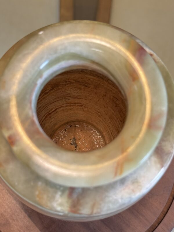 A close-up of the Woulind Chile Serving Dish shows its smooth, rounded rim and textured brown interior. The greenish-brown veined surface highlights the unique marble stone design and circular opening.