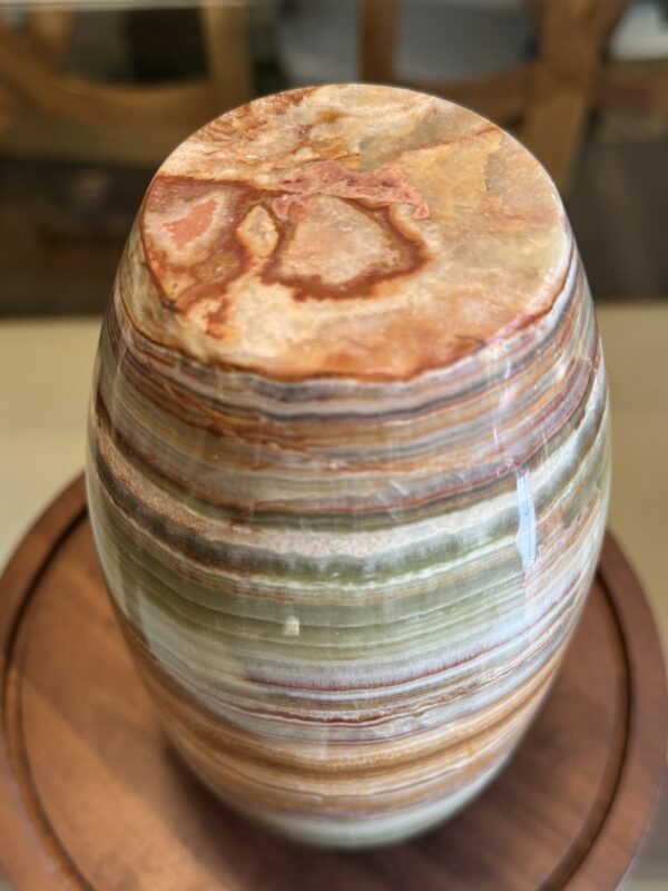 A polished, oval Woulind Chile Serving Dish features green, brown, cream, and reddish-orange horizontal layers with natural veins and a marbled effect. Its earthy charm makes it a striking centerpiece on any wooden surface.