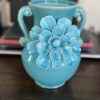 The Anding Crackle Glaze Decorative Vase, in turquoise with two curved handles and a large relief flower, brings elegance and charm to any setting, especially when displayed on a dark wooden table.