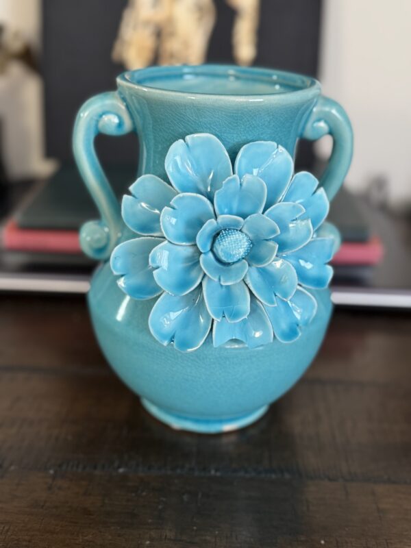 The Anding Crackle Glaze Decorative Vase, in turquoise with two curved handles and a large relief flower, brings elegance and charm to any setting, especially when displayed on a dark wooden table.