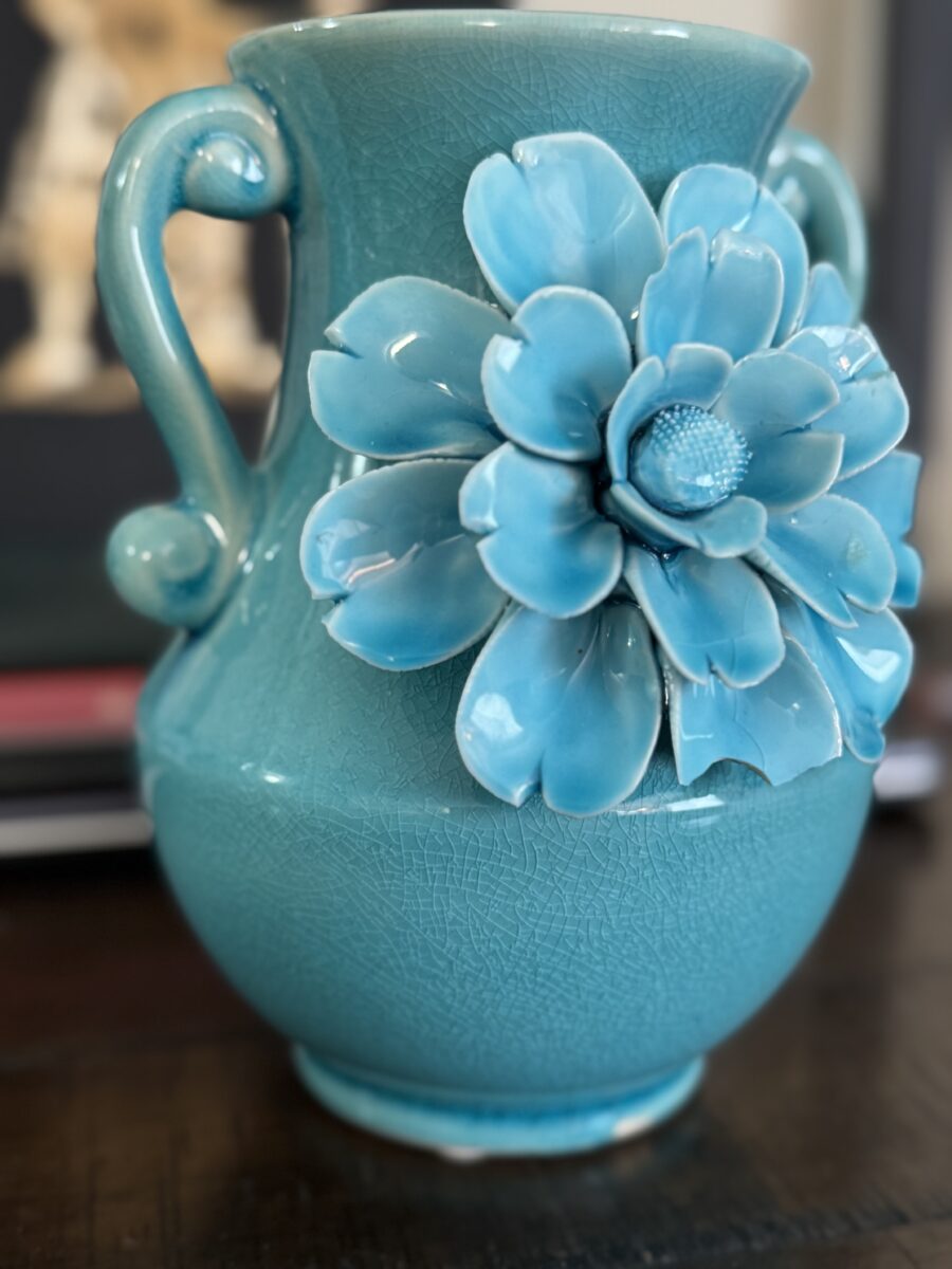 The Anding Crackle Glaze Decorative Vase features two curved handles and a large turquoise flower in relief, with a striking crackled finish. It sits on a dark surface against a softly blurred background.