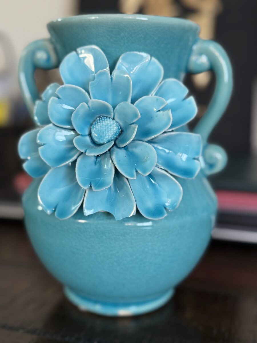 The Anding Crackle Glaze Decorative Vase in turquoise features two handles and a large relief flower on the front. Its glossy, layered petals match the vase, which is displayed on a dark surface with a blurred background.