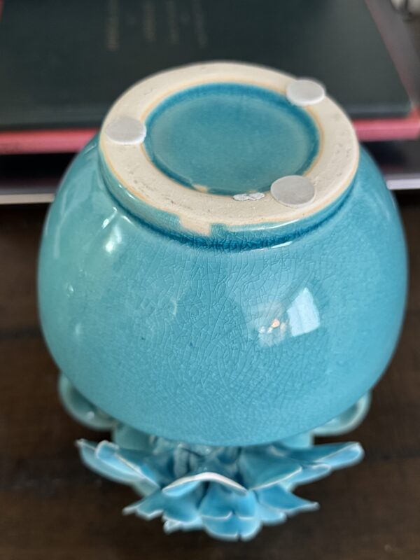 An Anding Crackle Glaze Decorative Vase is shown upside down, displaying four clear rubber pads on its base. Part of a ceramic flower and books are visible in the background.