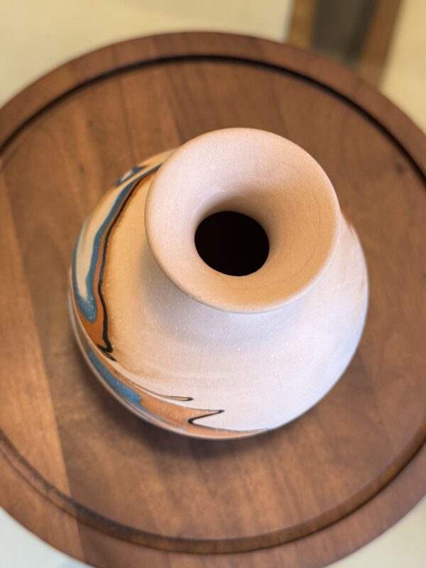 A small, round ceramic vase with beige, blue, black, and orange marbled swirls sits on a wooden tray beside the Woulind Chile Serving Dish, showcasing a handmade artistic look.