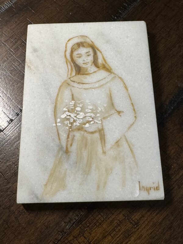 The Woulind Chile Serving Dish is a rectangular marble piece featuring a sepia-toned sketch of a woman in a long dress holding white flowers, with "Ingrid" inscribed in the lower right corner. It is displayed on a dark wooden surface.