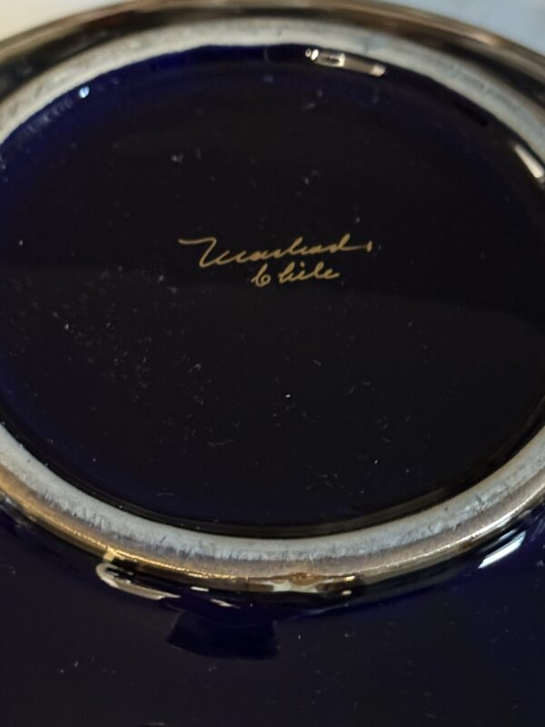 Close-up of the bottom of a dark blue ceramic plate with a glossy finish. At the center, “Villaruel, Chile” is handwritten in gold cursive script. The plate’s unglazed rim is visible, revealing a rough, grayish edge.