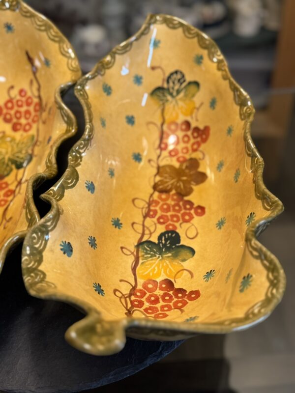 An Italian Oblong MCM Serving Dish shaped like a large leaf, glazed yellow with green edges and featuring red, orange, and blue hand-painted floral details. A second matching dish is partially visible next to it.