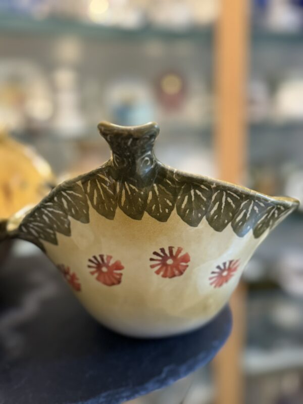 This cream Italian Oblong MCM Serving Dish features a leaf-patterned rim, sculpted bird head, green leaves, and red floral accents—displayed in front of blurred shelves with other MCM serving dishes.