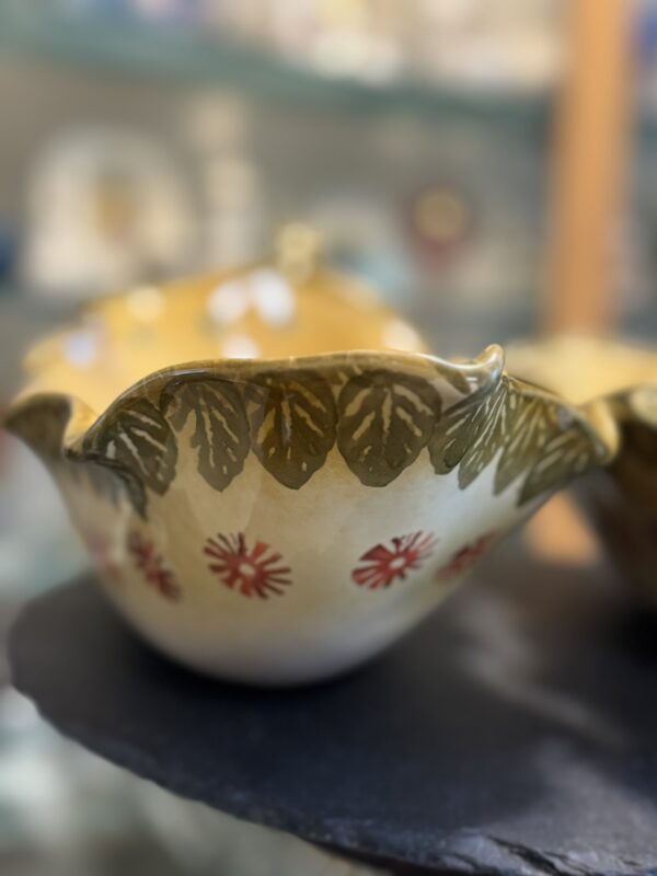 The Italian Oblong MCM Serving Dish features a wavy rim, painted green leaves, and red floral motifs on cream with a yellow interior—a decorative ceramic piece inspired by Italian design, perfect for serving.