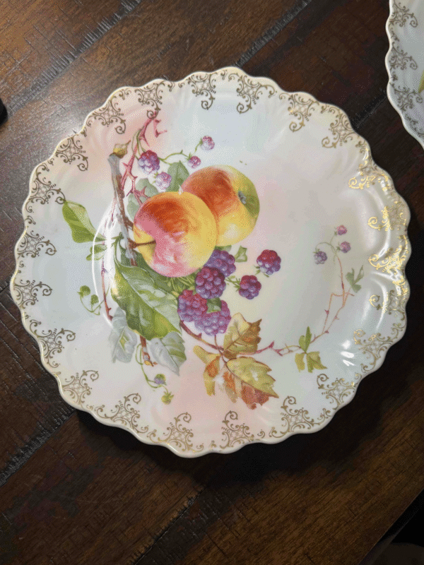 A Zeh Scherzer Bavarian Plate: Punch, Peach with scalloped edges, gold trim, and a hand-painted design of peaches and berries rests on a dark wooden surface.