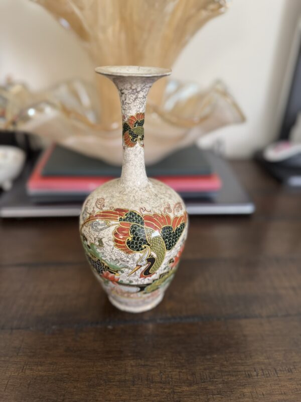 The Chinese Blue & White Miniature Vase, with its slender shape and narrow neck, displays an intricate design of birds and flowers. It rests on a wooden table, with blurred books and a glass bowl in the background.