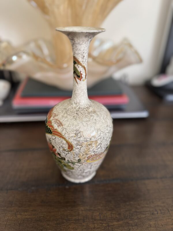 A Chinese Blue & White Miniature Vase with intricate floral and leaf designs stands on a wooden table, accented by a blurred decorative glass piece and stacked books in the background. The vase has a vintage, ornate look.