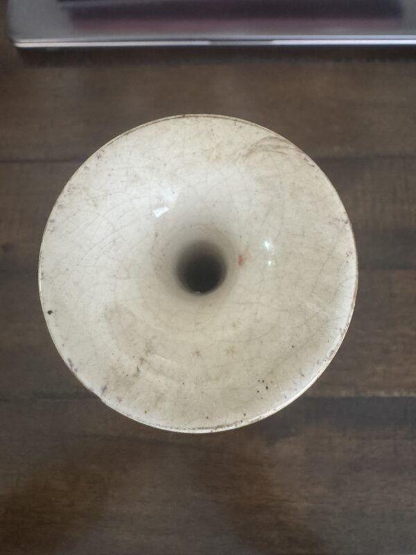 A top-down view of the Chinese Blue & White Miniature Vase, round and white with a narrow dark central opening, visible glaze crackling, and a slightly worn, discolored rim, displayed on a wooden surface.