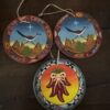 Three round, hand-painted ornaments sit on wood: two show roadrunners in desert scenes with cacti and stars, bordered by geometric patterns inspired by the Chinese Blue & White Miniature Vase; the third features red chili peppers on yellow-orange.