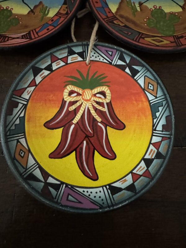 A round decorative plate showcases five red chili peppers with a yellow bow on a yellow-orange background. The border has Southwestern patterns and features a tiny Chinese Blue & White Miniature Vase motif in black, white, red, and purple.