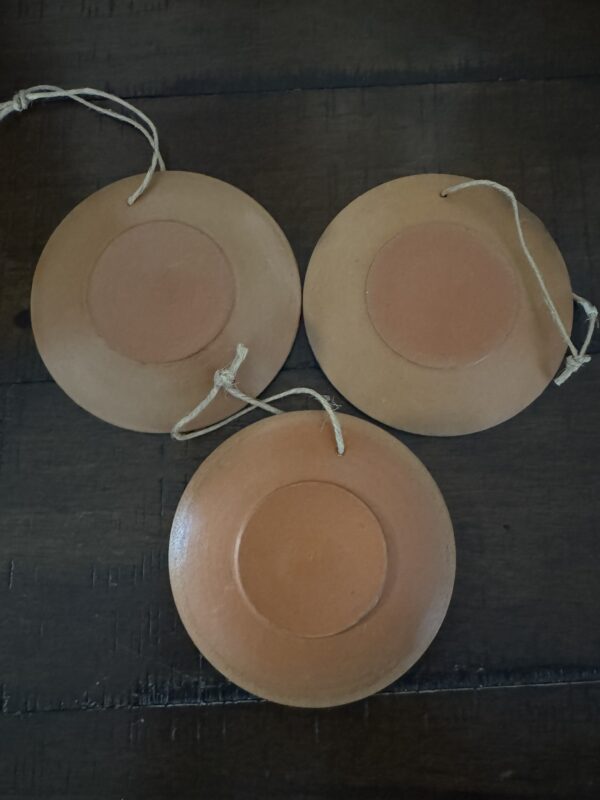 Three small, flat, clay-colored discs with raised centers are arranged in a triangle on a dark wood surface. Each has an attached string and features designs inspired by the Chinese Blue & White Miniature Vase.