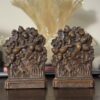 Two ornate bronze bookends with oak leaf and acorn detail sit on a wooden surface. Behind them is a Chinese Blue & White Miniature Vase, its elegant design recalling classic Chinese artistry.